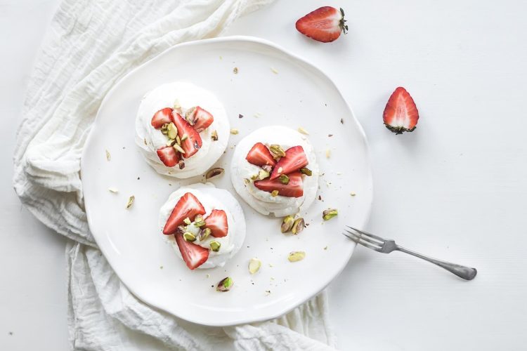 small strawberry and pistachio pavlova meringue cakes with mascarpone cream, fresh mint over white backdrop