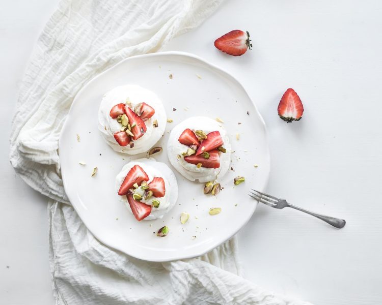 small strawberry and pistachio pavlova meringue cakes with mascarpone cream, fresh mint over white backdrop