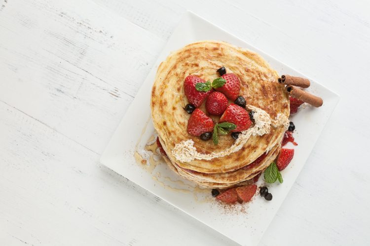 white plate full of pancakes with raspberries strawberries blueberries and honey