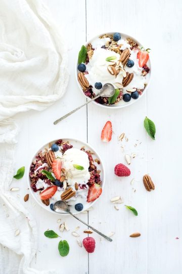 healthy breakfast. berry crumble with fresh blueberries, raspberries, strawberries, almond, walnuts, pecans, yogurt, and mint in ceramic plates over white wooden surface