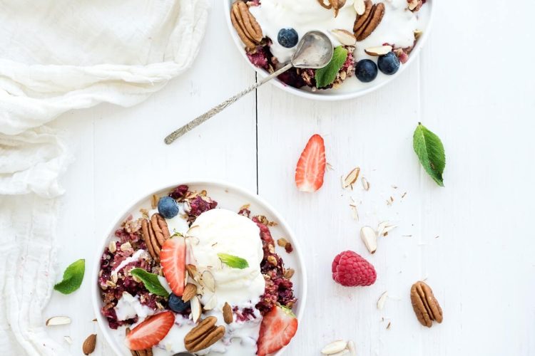 healthy breakfast. berry crumble with fresh blueberries, raspberries, strawberries, almond, walnuts, pecans, yogurt, and mint in ceramic plates over white wooden surface